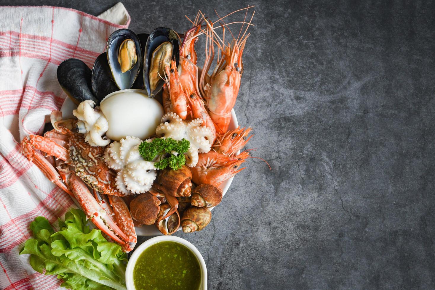 Fresh shrimps prawns squid mussels  spotted babylon shellfish crab and seafood sauce lemon on plate black stone background top view copy space - Cooked steamer food served seafood buffet concept photo