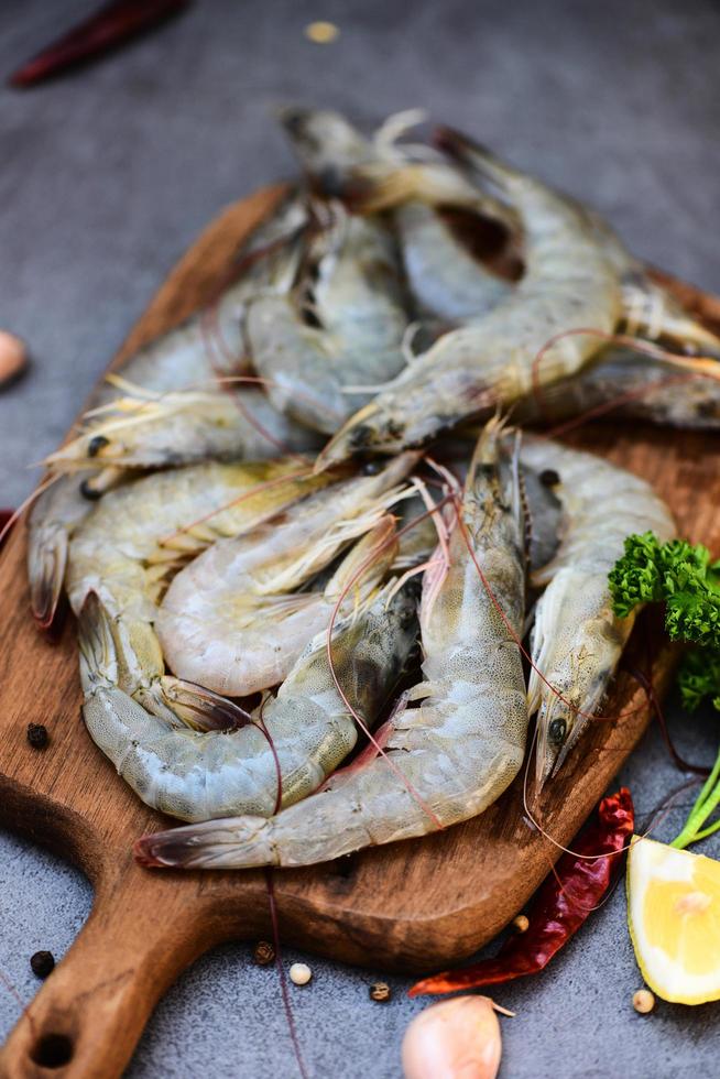 langostinos frescos para cocinar con especias limón ajo pimienta negra chile en tabla de cortar de madera en el restaurante de mariscos, camarones crudos en plato oscuro foto