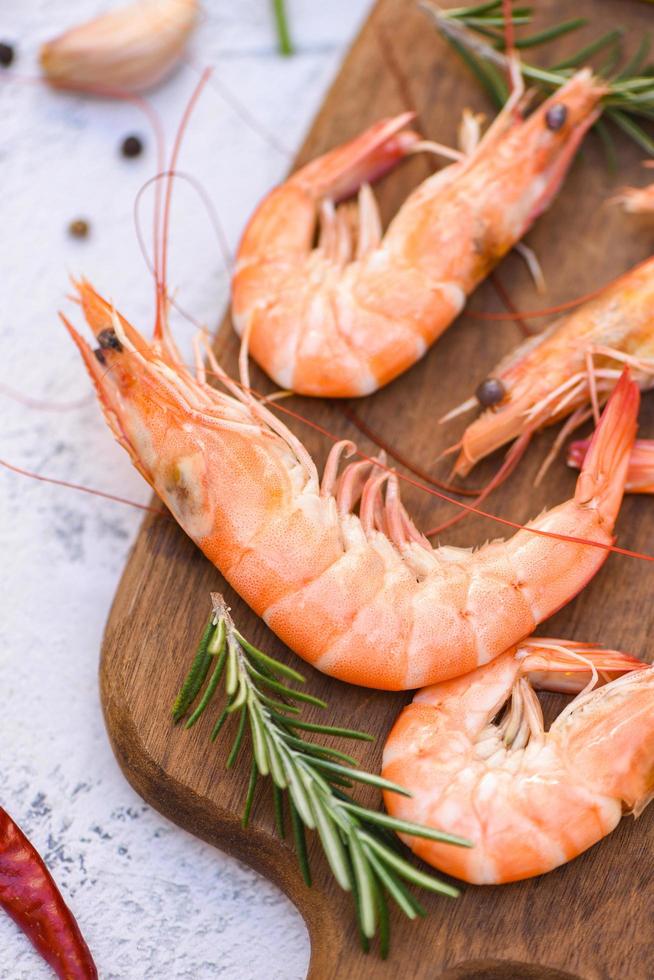 boiled shrimp prawns cooked in the seafood restaurant, fresh shrimps wooden cutting board plate with ice herbs and spices lemon chili rosemary on table background photo