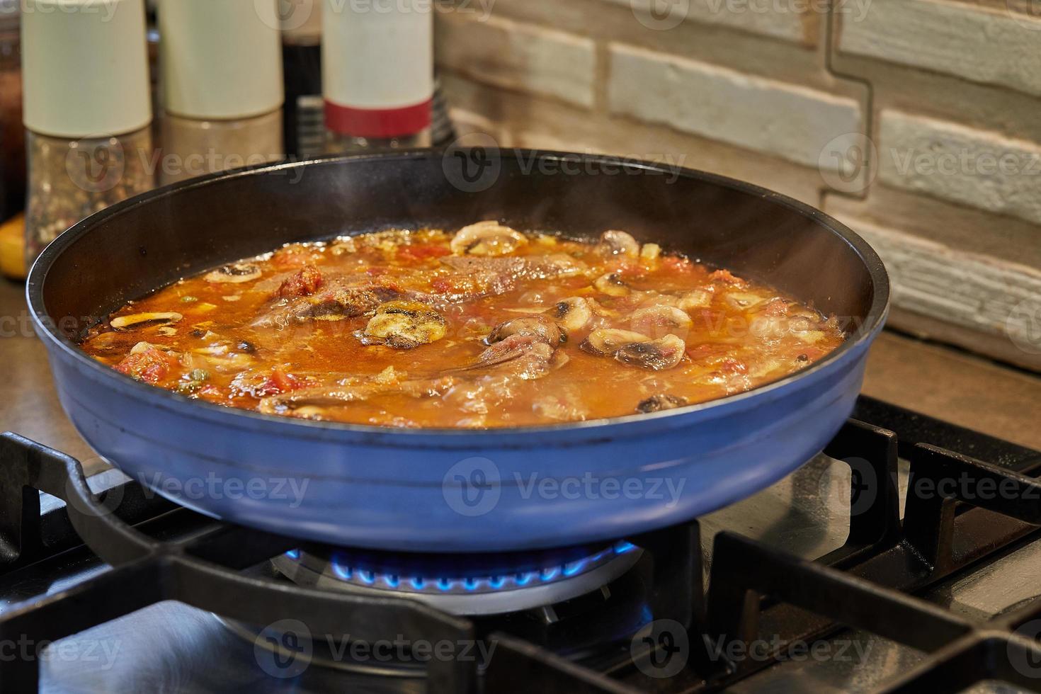 Veal tongue with tomato sauce, mushrooms and capers is fried in frying pan on gas stove. French gourmet cuisine photo