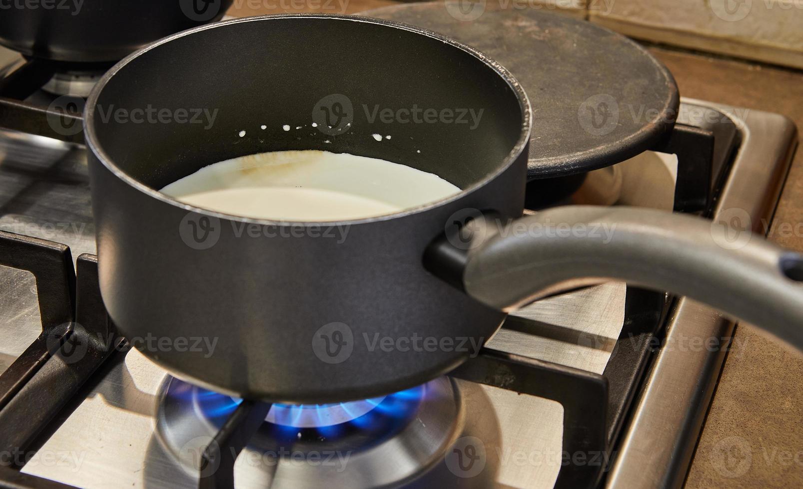 Cream is cooked in saucepan on gas stove to make cake photo