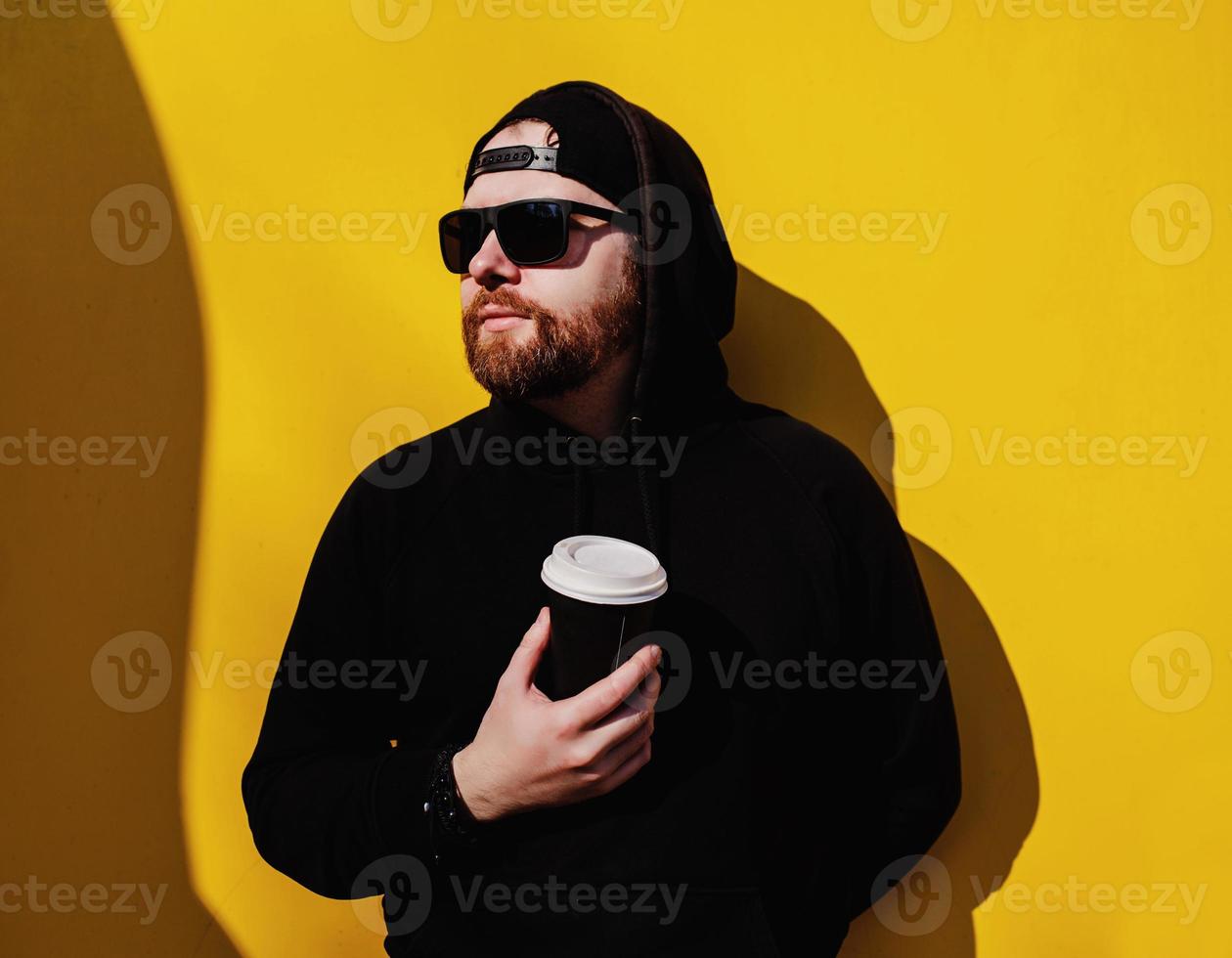 man in hoodie standing with coffee to go photo