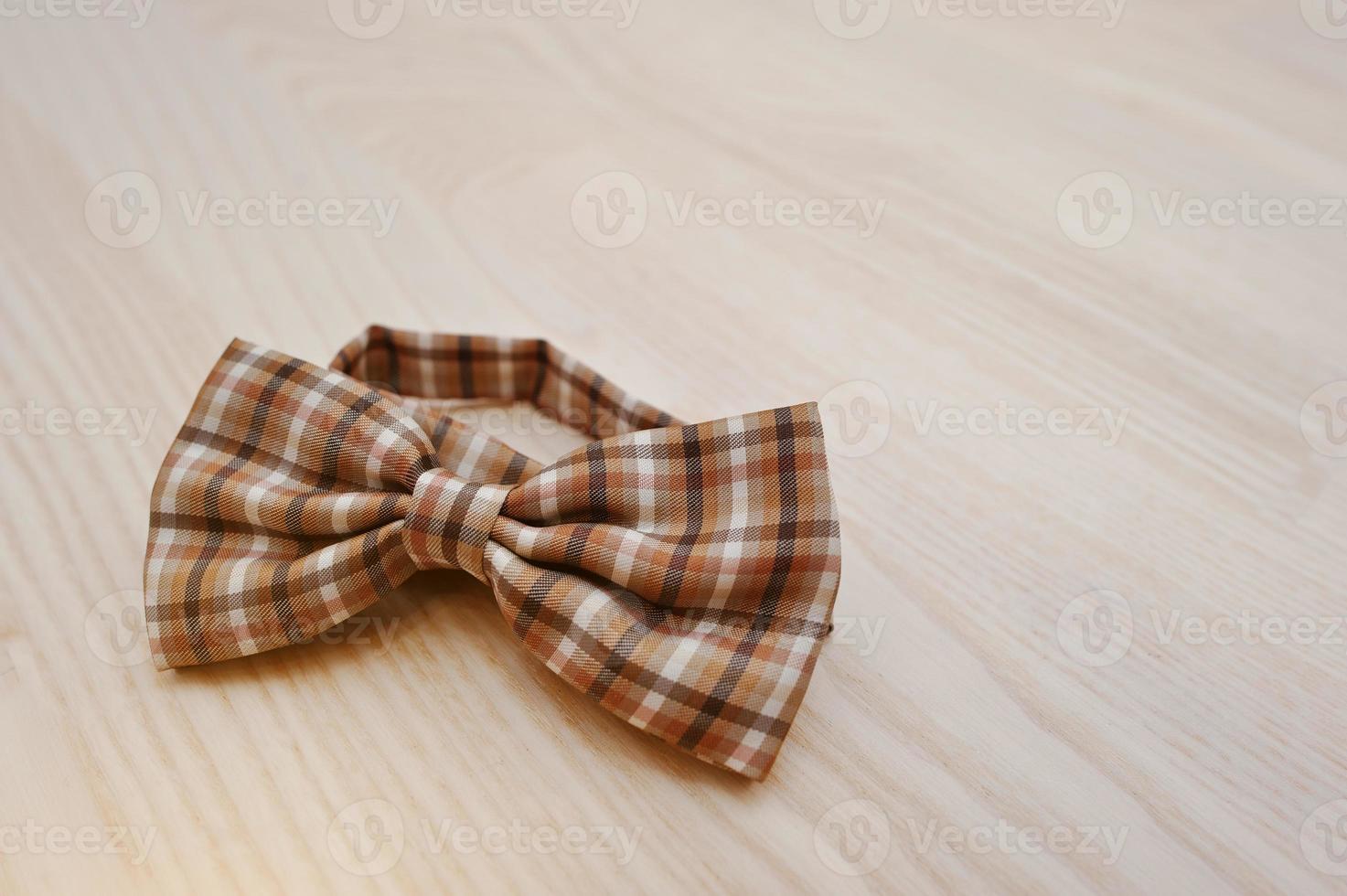 Brown checkered bow tie on light wooden background photo