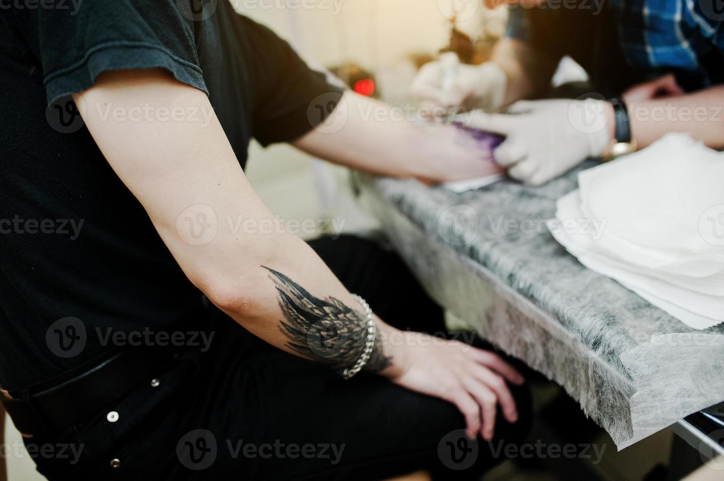 el maestro del tatuaje hace un tatuaje para un hombre rockero en el salón de tatuajes foto