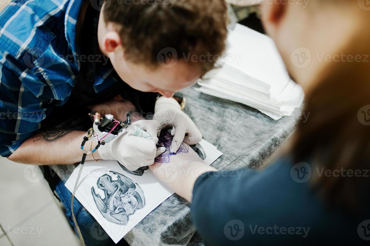 el maestro del tatuaje hace un tatuaje para un hombre rockero en el salón de tatuajes foto