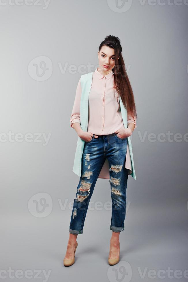Full-length portrait young brunette girl wearing in pink blouse, turquoise jacket, ripped jeans and cream shoes .Fashion studio shot photo