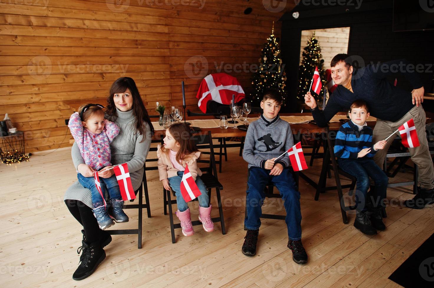 Family with Denmark flags inside wooden house sitting by table. Travel to Scandinavian countries. Happiest danish people's . photo