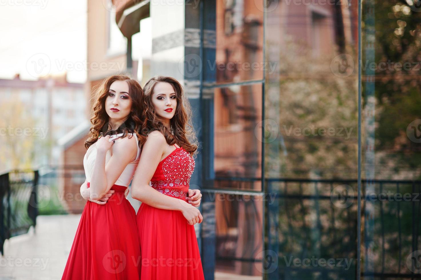 retrato de dos chicas de moda con vestido de noche rojo posado en la ventana de espejo de fondo de un edificio moderno foto