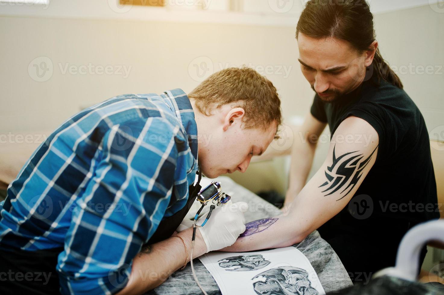 el maestro del tatuaje hace un tatuaje para un hombre rockero en el salón de tatuajes foto