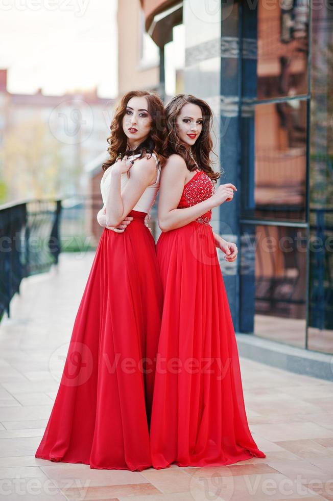 retrato de dos chicas de moda con vestido de noche rojo posado en la ventana de espejo de fondo de un edificio moderno foto