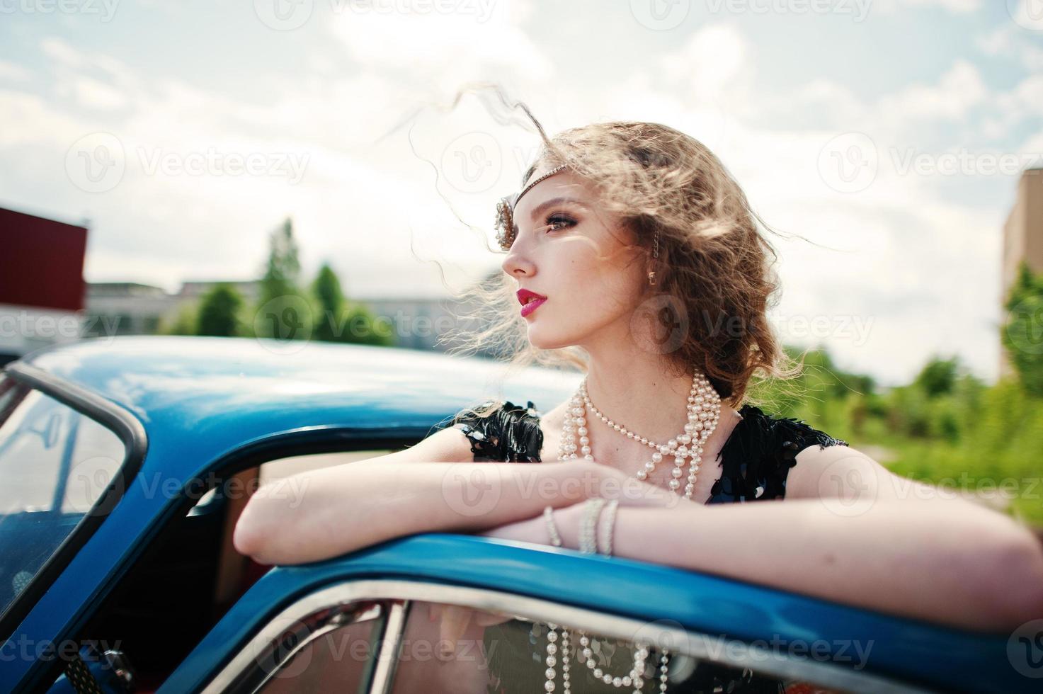 Portrait of beautiful curly fashion girl model with bright makeup in retro style leaned on a vintage car door. photo