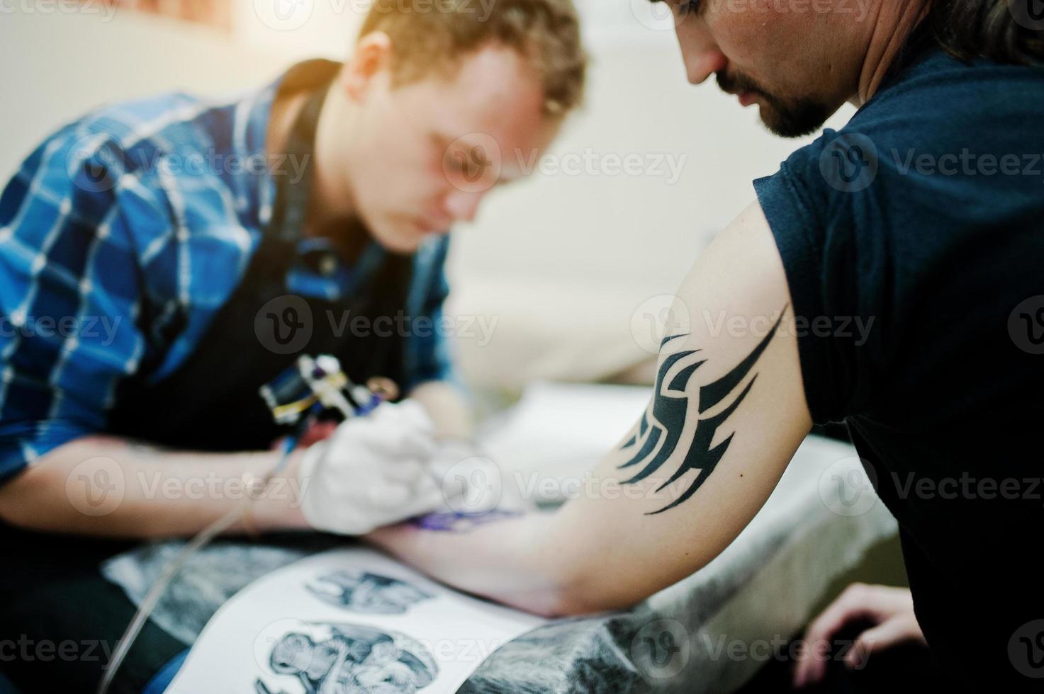 Tattoo master make tattoo for rocker man at tattoo salon photo