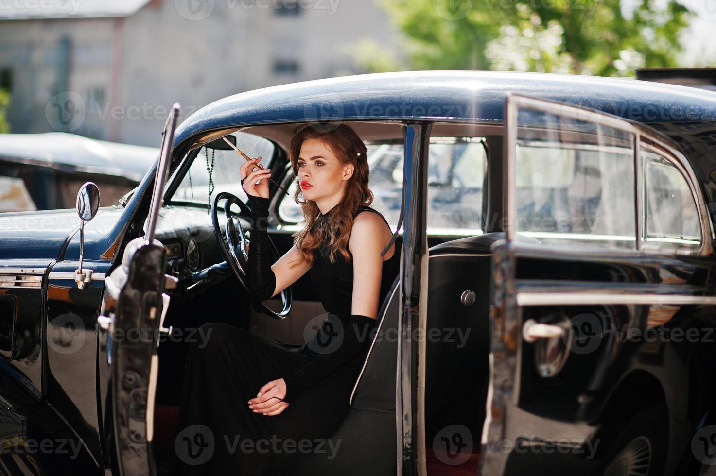 Portrait of beautiful sexy fashion girl model with bright makeup in retro style sitting in vintage car with a cigarette in hand. photo