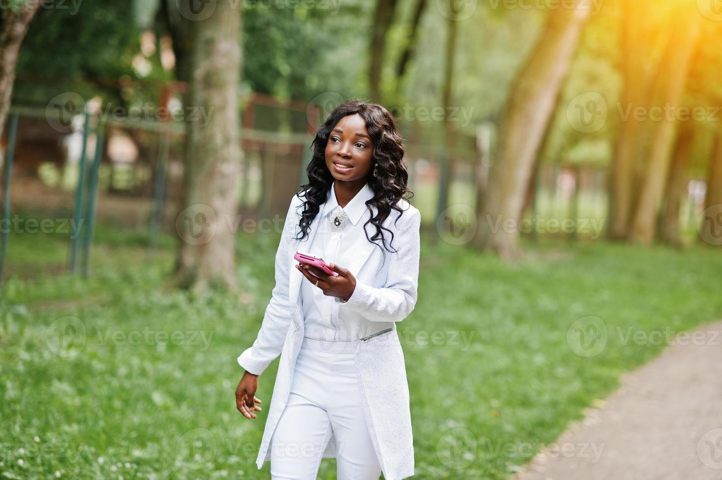 Stylish black african american girl walking on park with mobile phone at hand photo