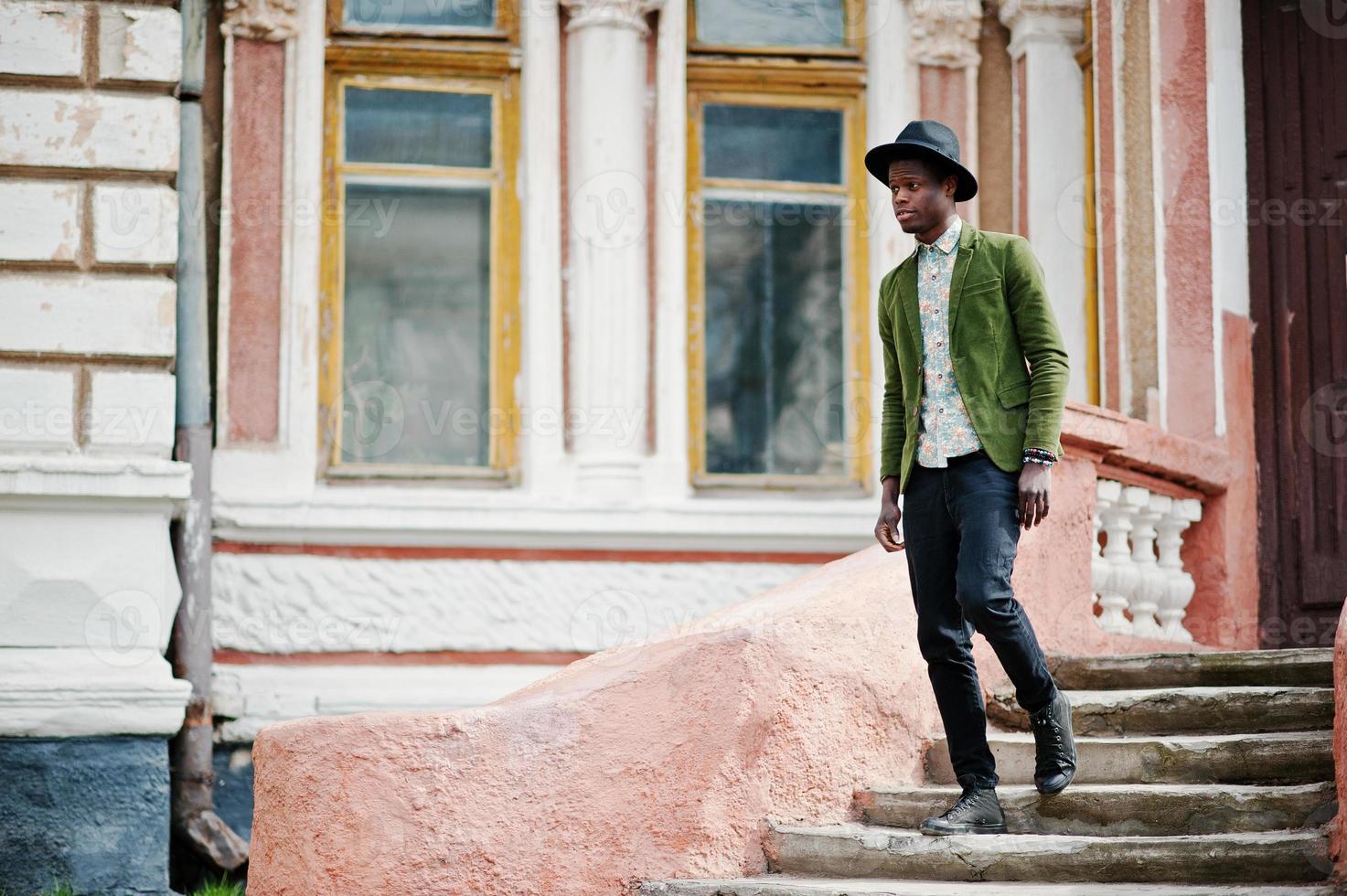 Fashion portrait of black african american man on green velvet jacket and black hat stay on stairs background old mansion. photo