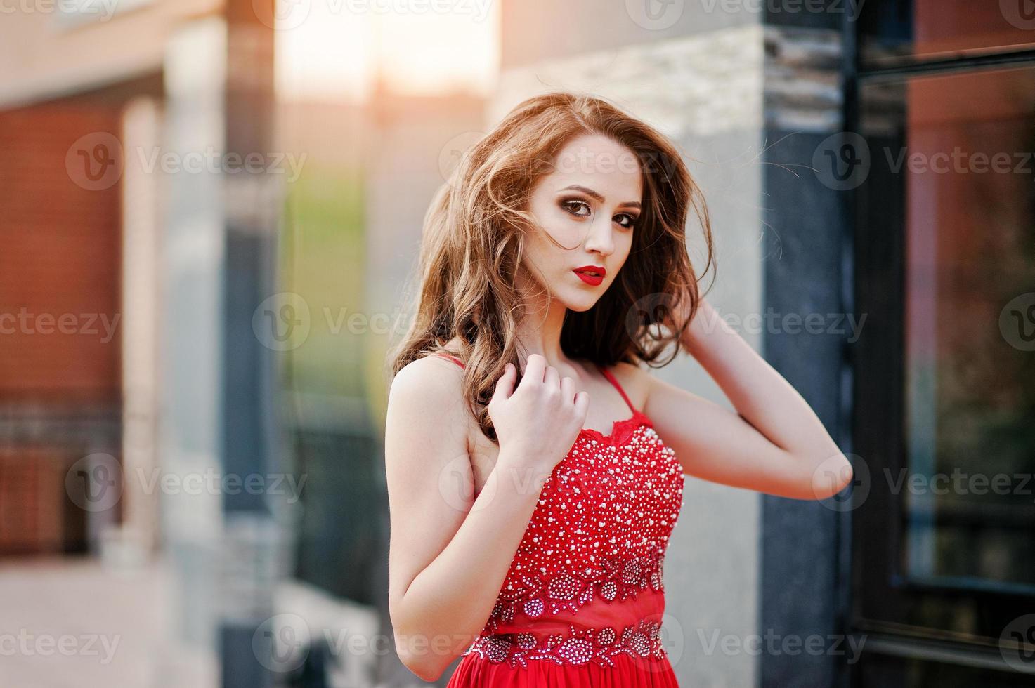 Close up portrait of fashionable girl at red evening dress posed background mirror window of modern building photo