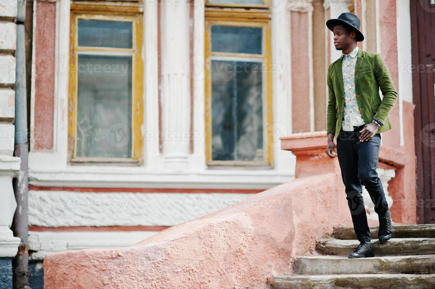 Fashion portrait of black african american man on green velvet jacket and black hat stay on stairs background old mansion. photo