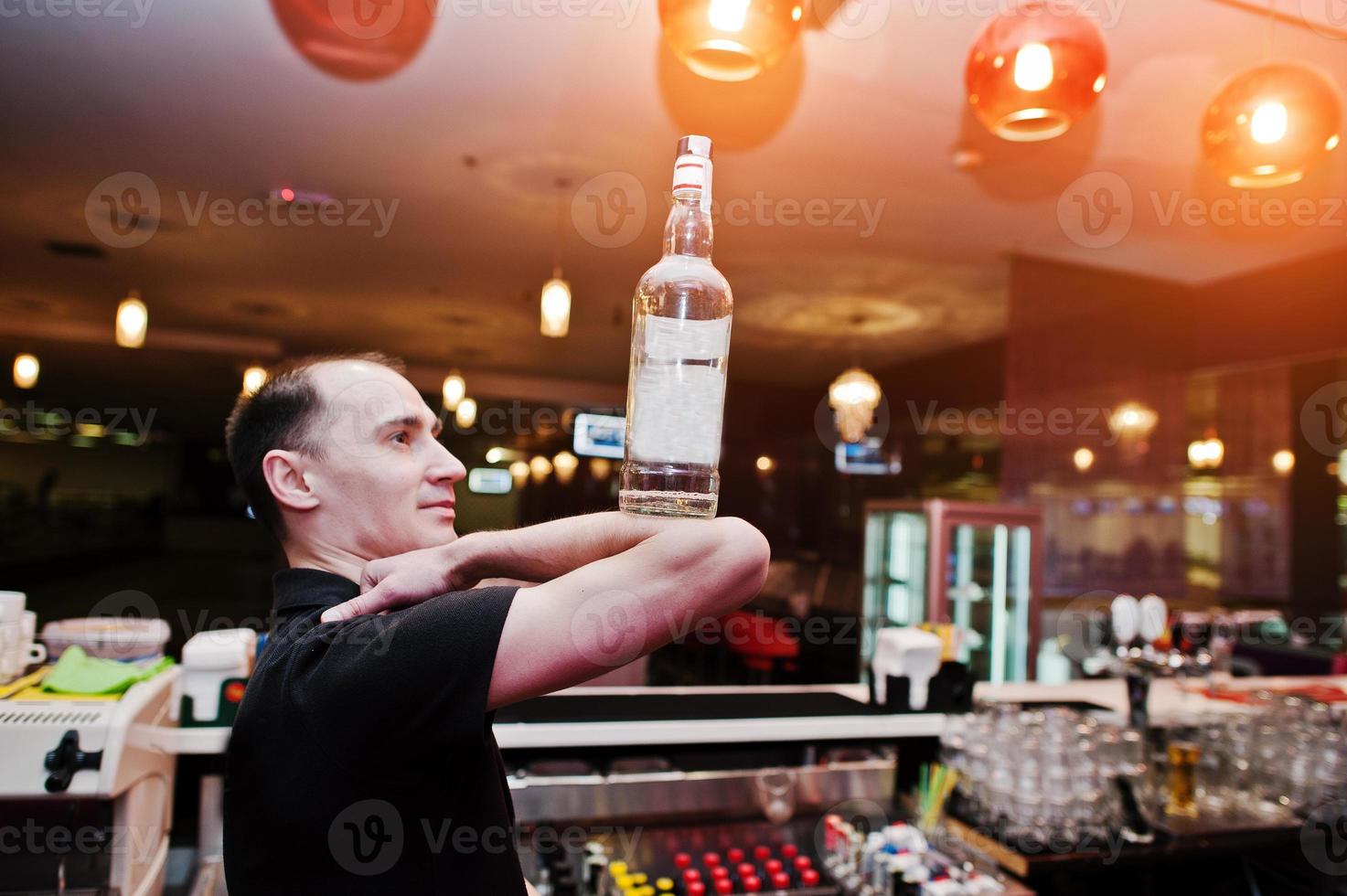 Barman hold bottle on elbows of hand at the bar photo