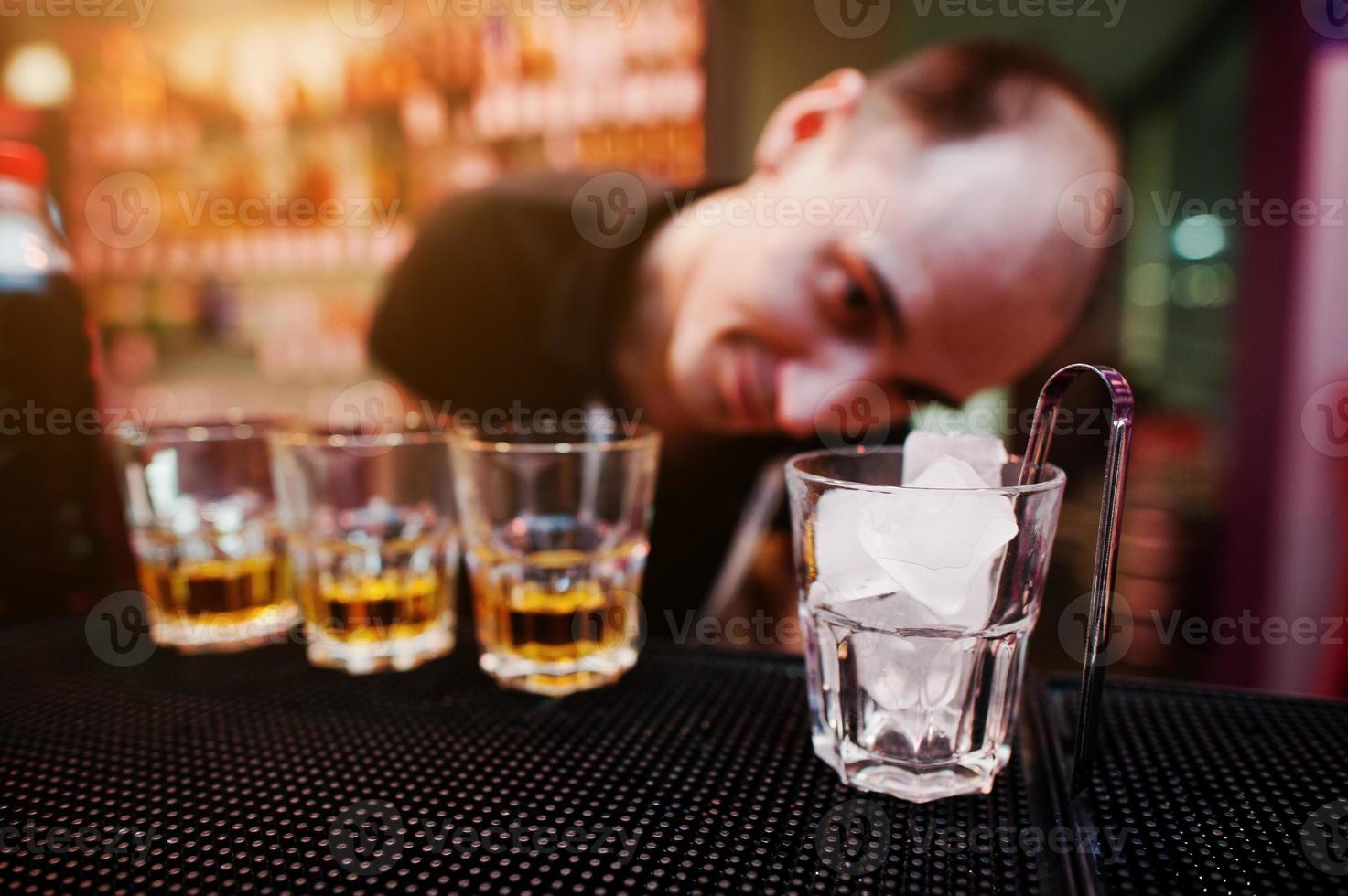 vaso con hielo y pinzas con tres vasos de whisky fondo divertido barman foto