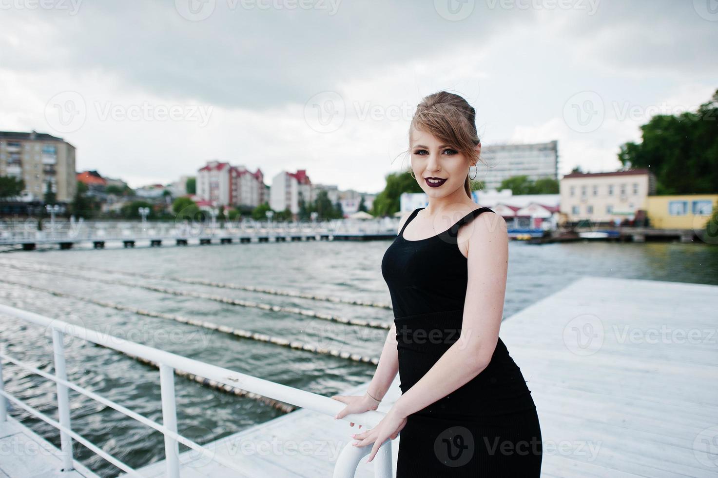 chica joven con vestido negro y labios negros posados en el muelle foto