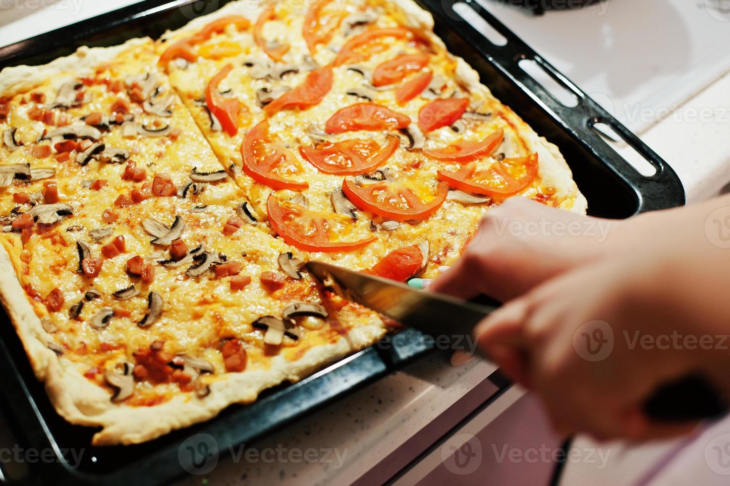 mujer cortada con un cuchillo pizza casera en la cocina foto