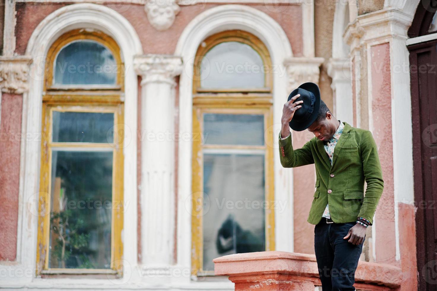 Fashion portrait of black african american man on green velvet jacket stay on stairs and wear his black hat background old mansion. photo