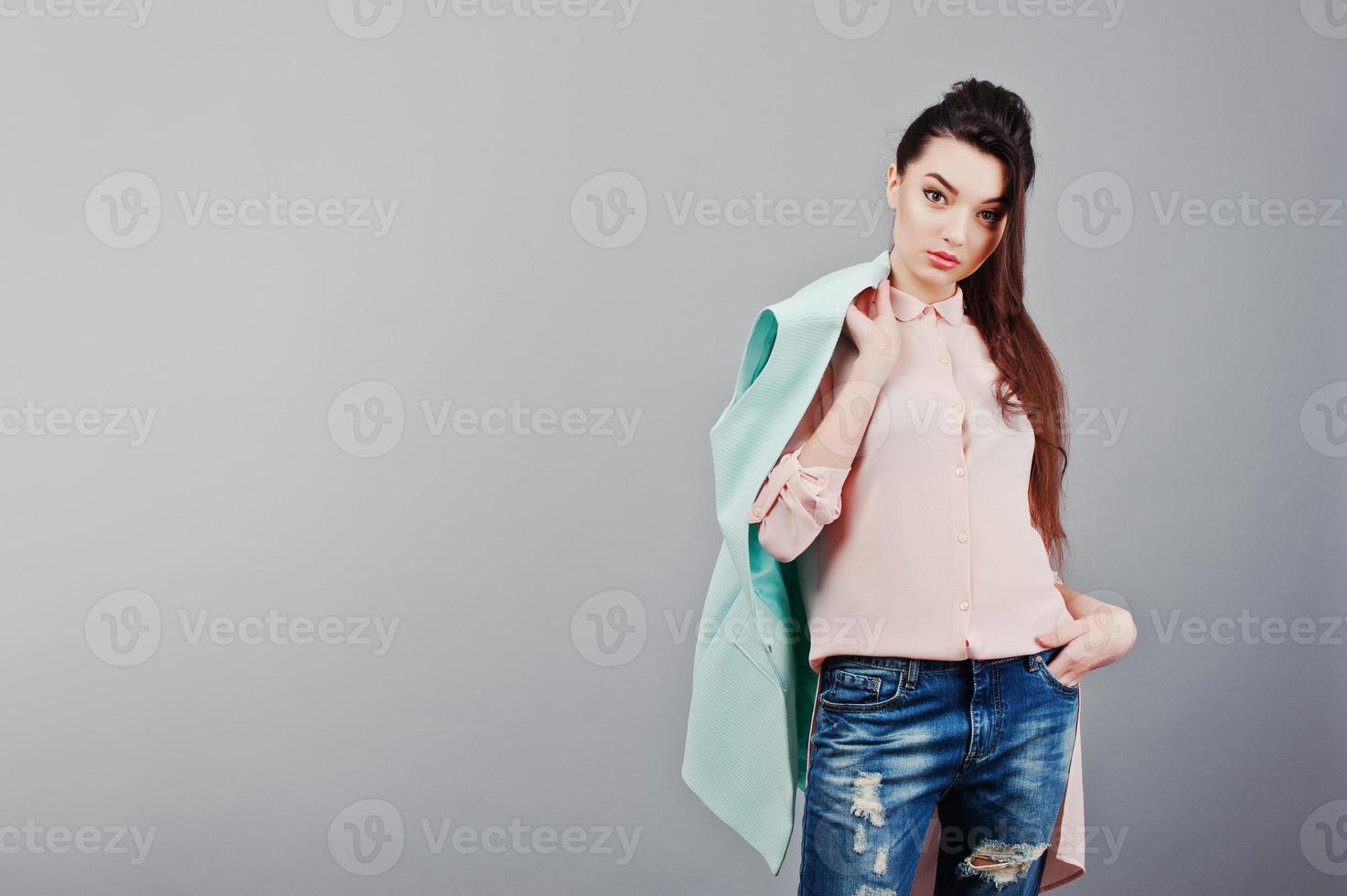 Portrait of young brunette girl wearing in pink blouse, turquoise jacket, ripped jeans. Fashion studio shot photo