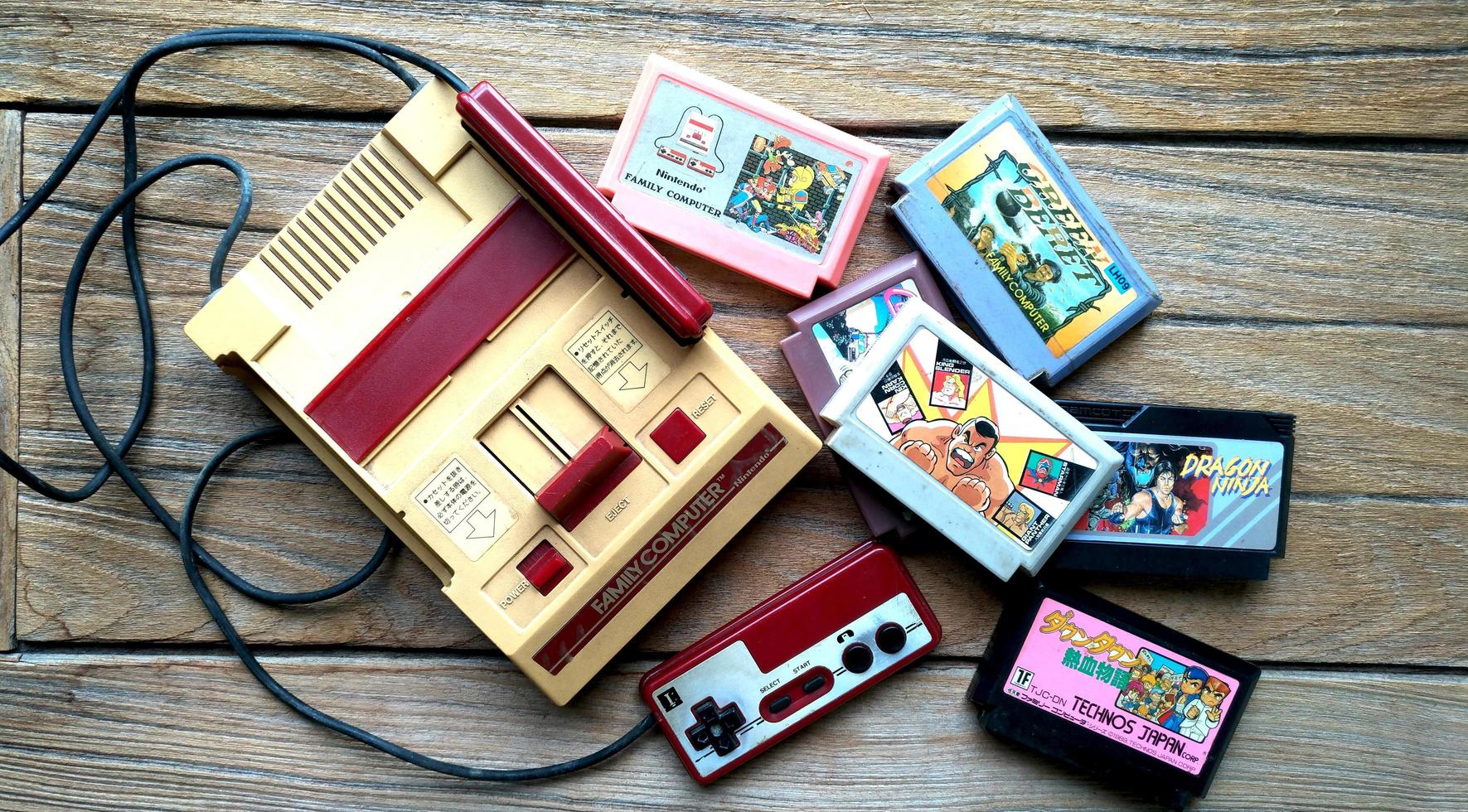 bangkok, tailandia - 10 de abril de 2019. antiguo sistema de entretenimiento nintendo computadora familiar y cartuchos de juego sobre fondo de madera. foto