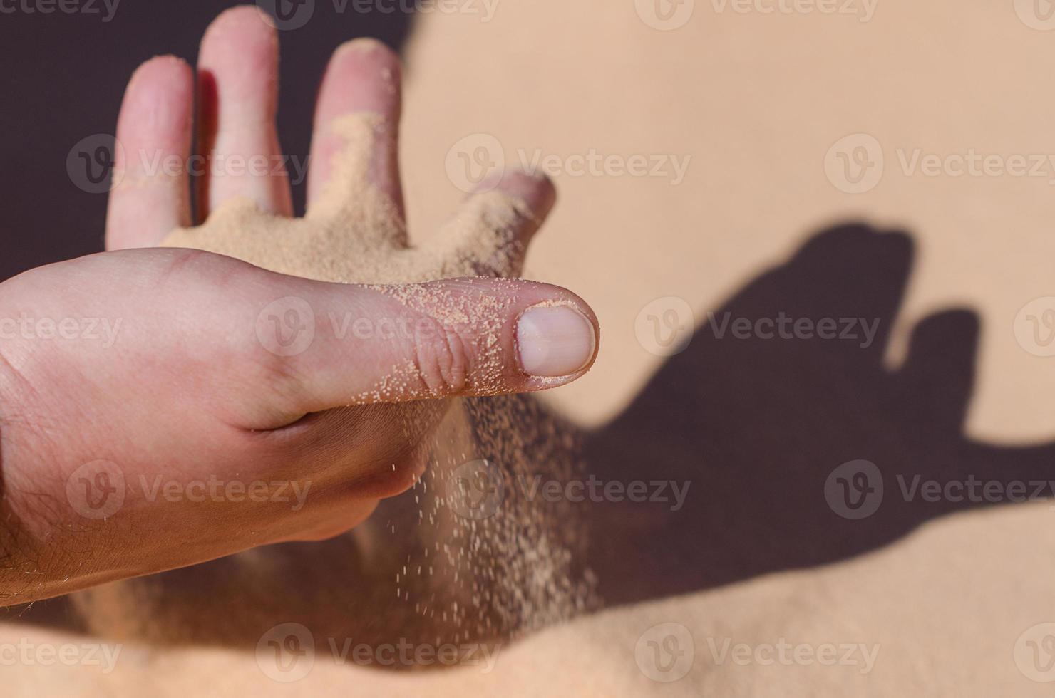 Desert. Sunny day. Sand pours through the fingers of a man. Vacation concept. photo