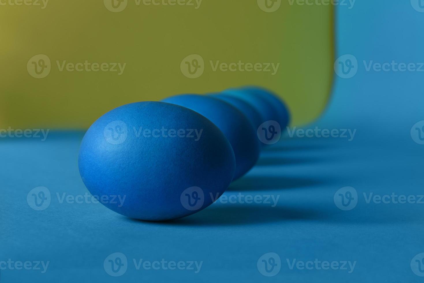 Five blue painted Easter eggs lie diagonally on a blue and yellow background. Deep shadows. photo
