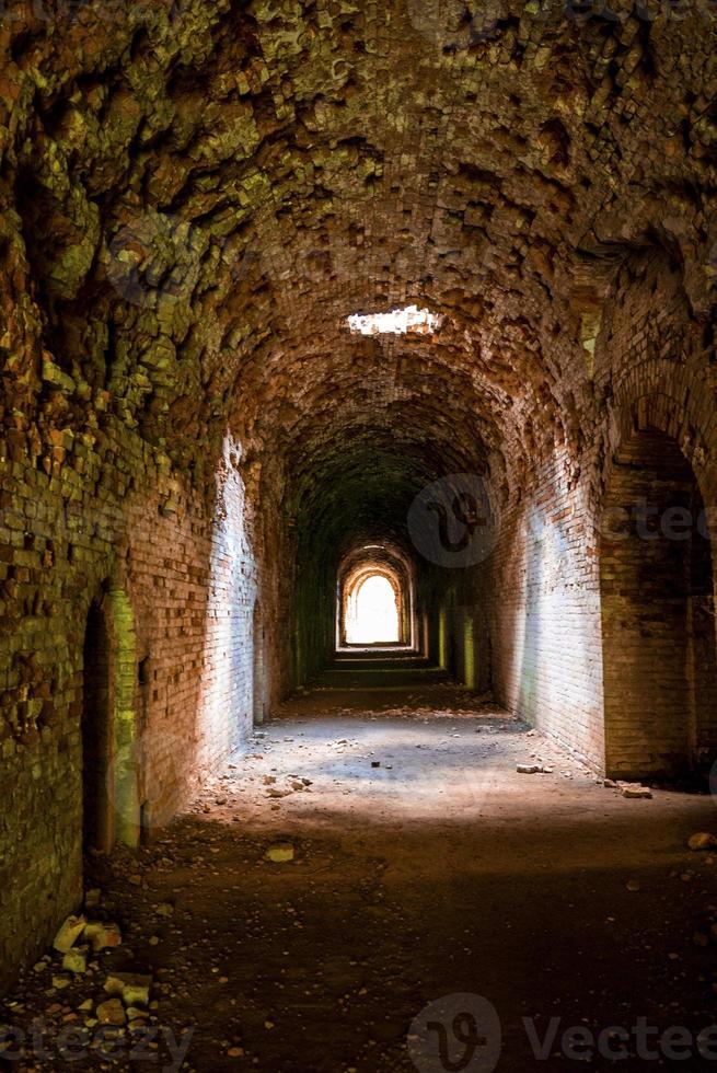 Sunlight shines through hole from brick ceiling in passage of old abandoned fort photo