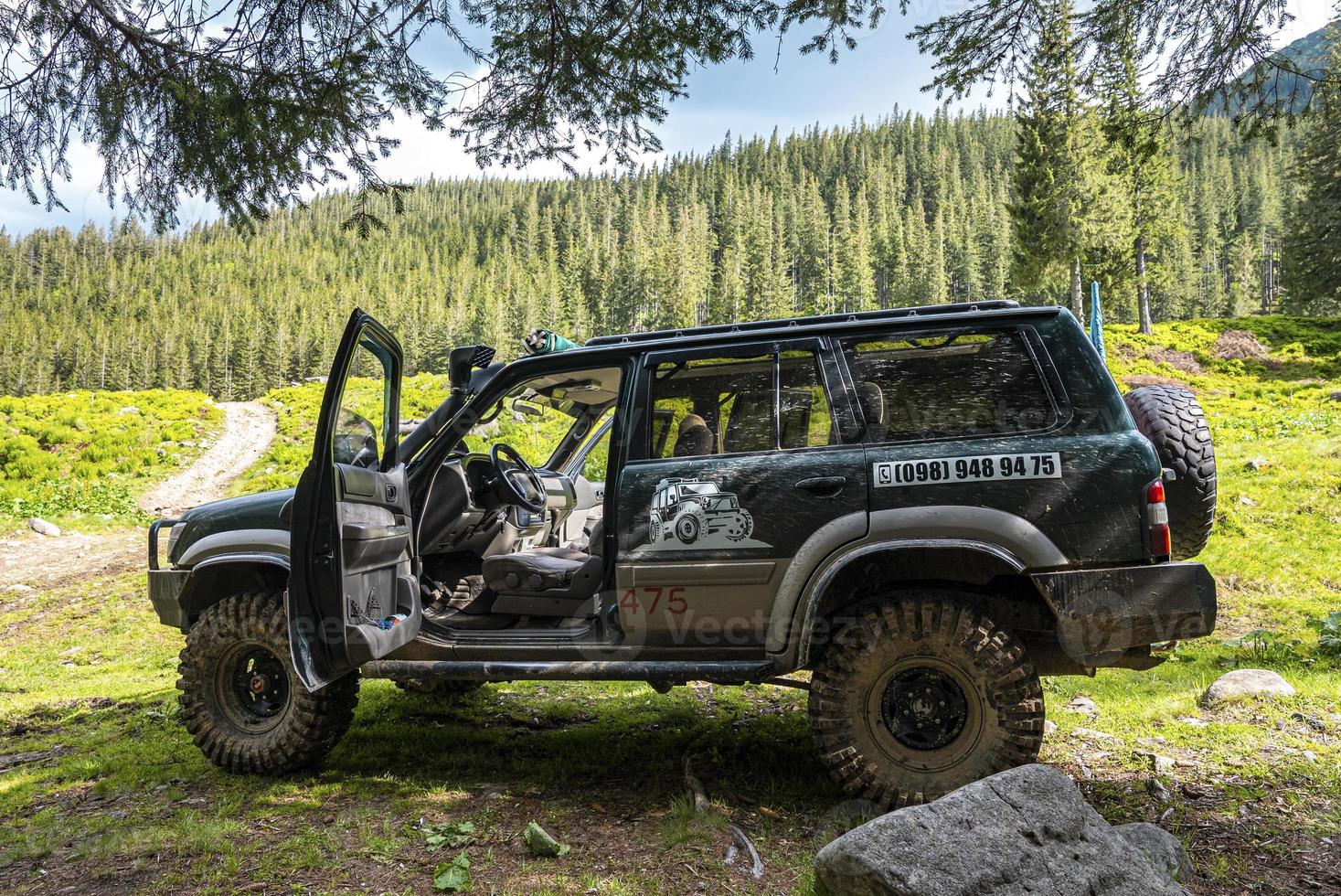 todoterreno 4x4 con puerta abierta bajo un árbol contra un denso bosque. foto