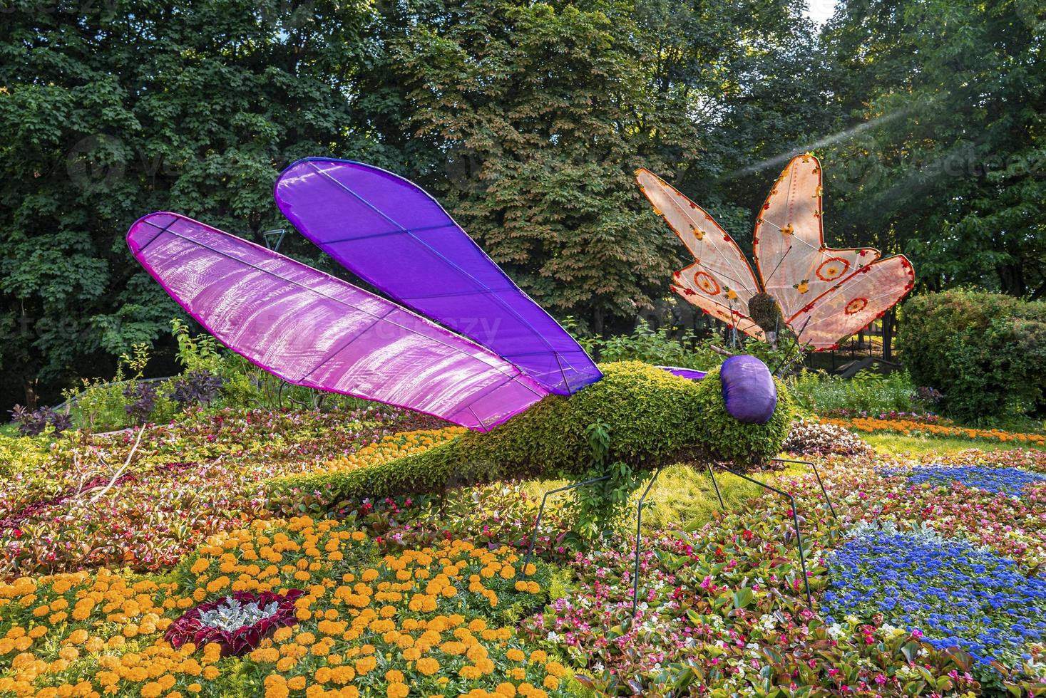 figura de mariposa y libélula de pie en una exposición de flores coloridas en el jardín foto