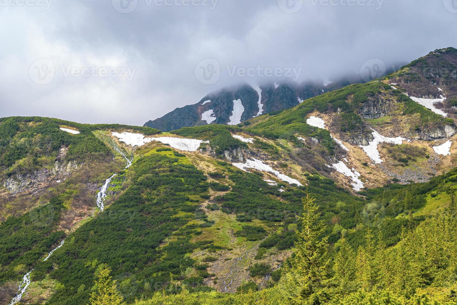 Snow covered mountain slope and waterfall against cloudy sky photo