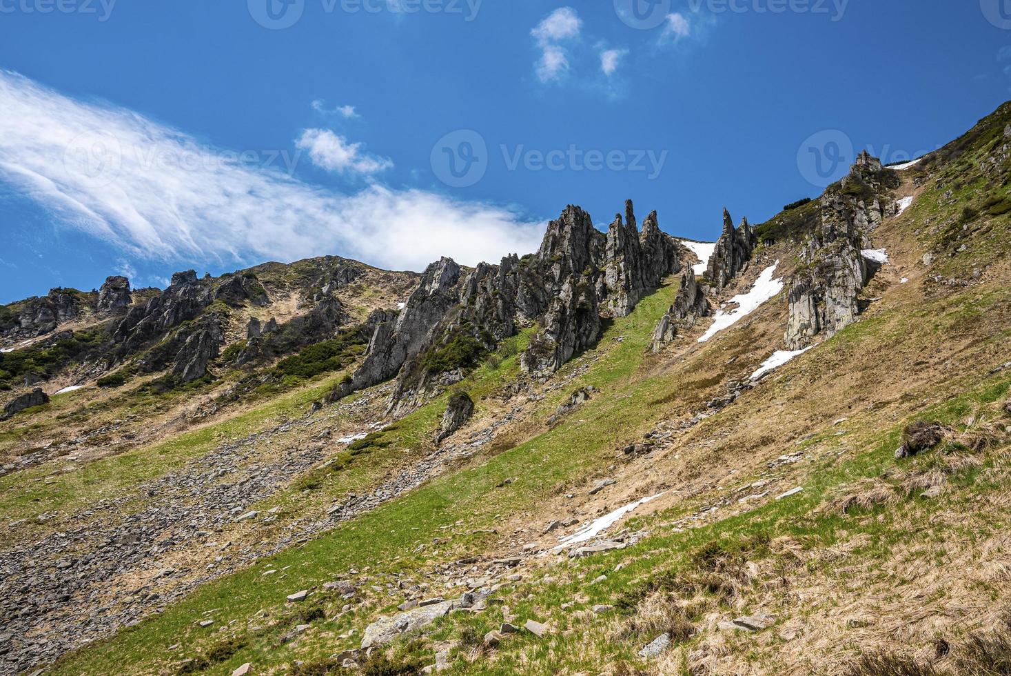Rock cliff covered with moss and snow over steep slope against sky photo