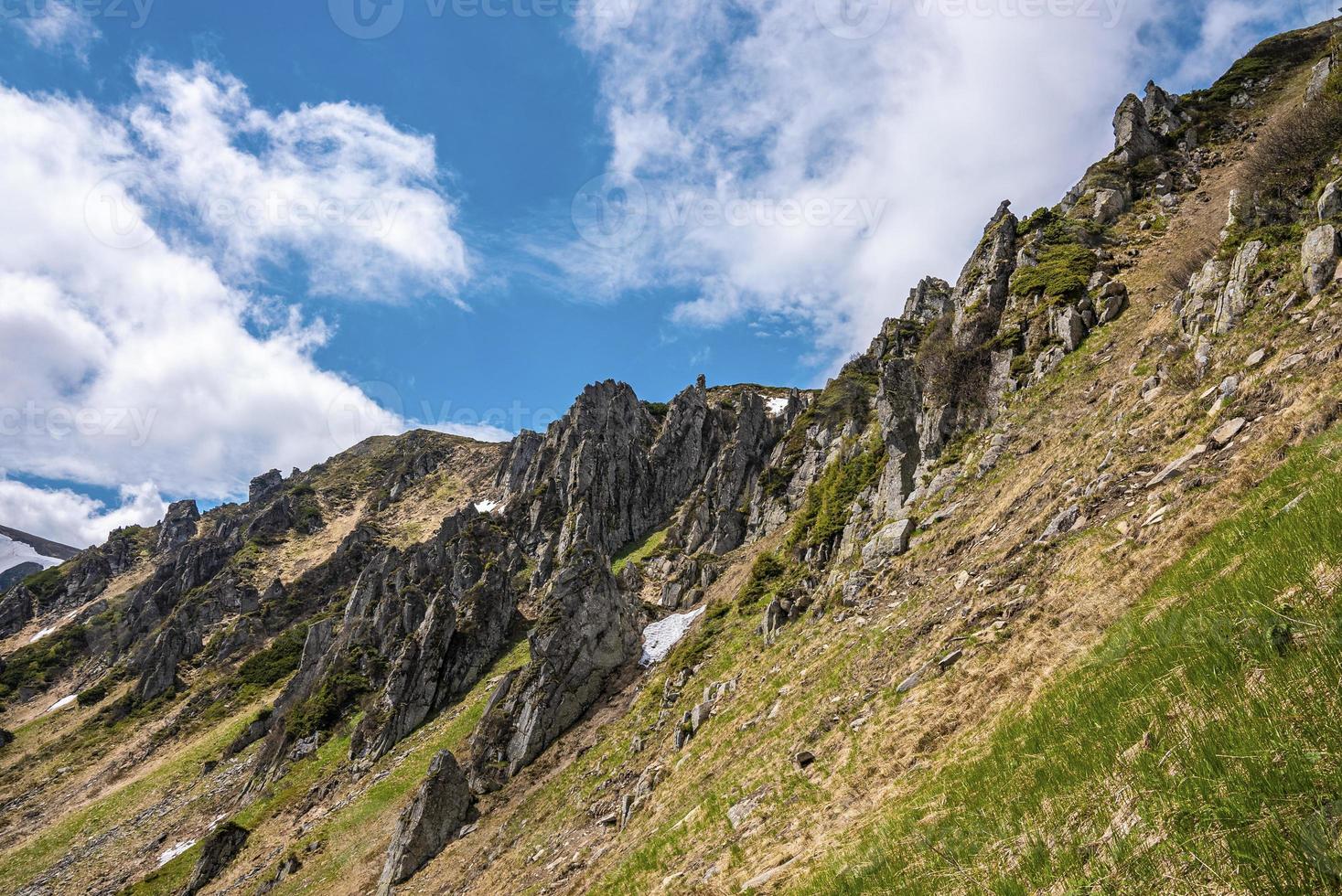 Rock cliff covered with moss over steep slope against cloudy sky photo
