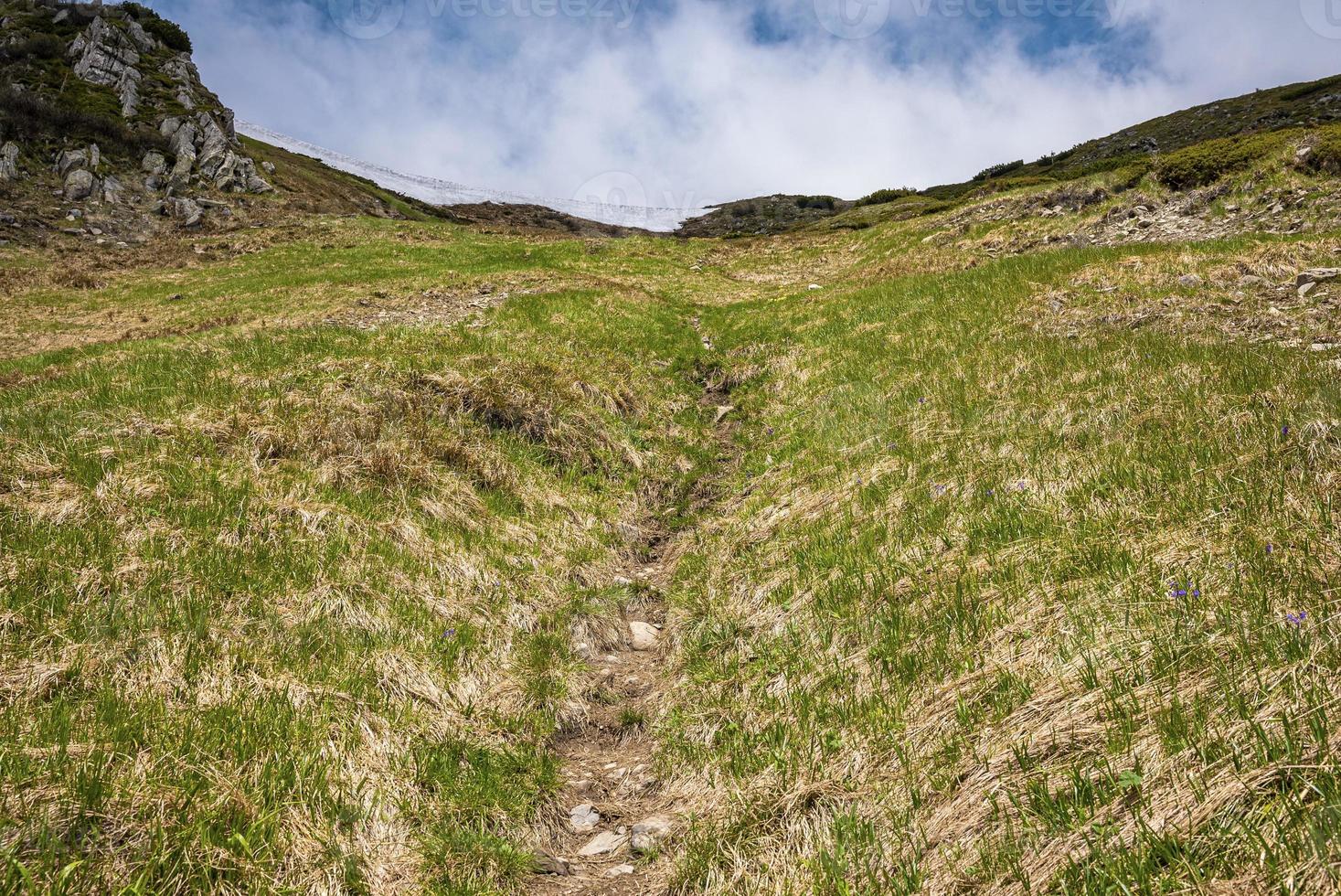 Low angle view of grass covered slope with path towards mountain photo