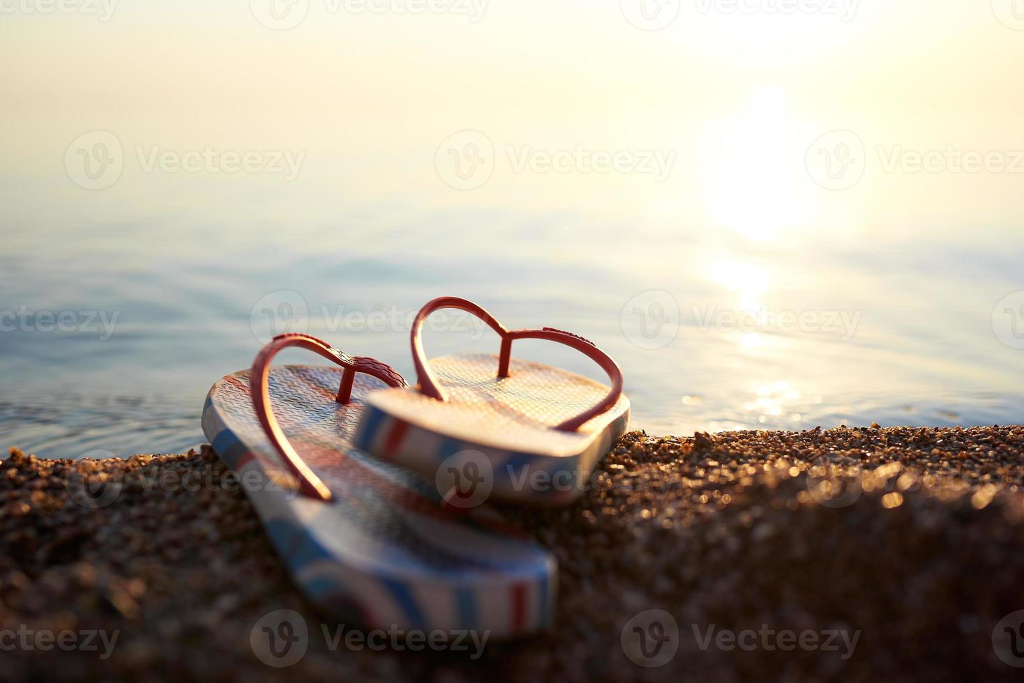 Beach flip-flops on a pebble beach close-up against the sea in a blur. The concept of beach holiday after pandemic. photo