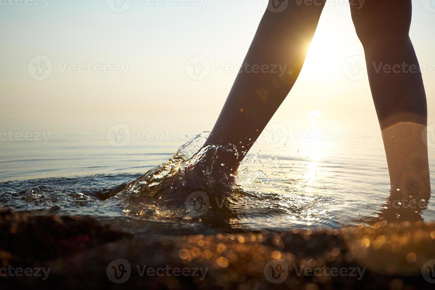 los pies descalzos de las mujeres caminan sobre el agua iluminada por la luz del sol. foto