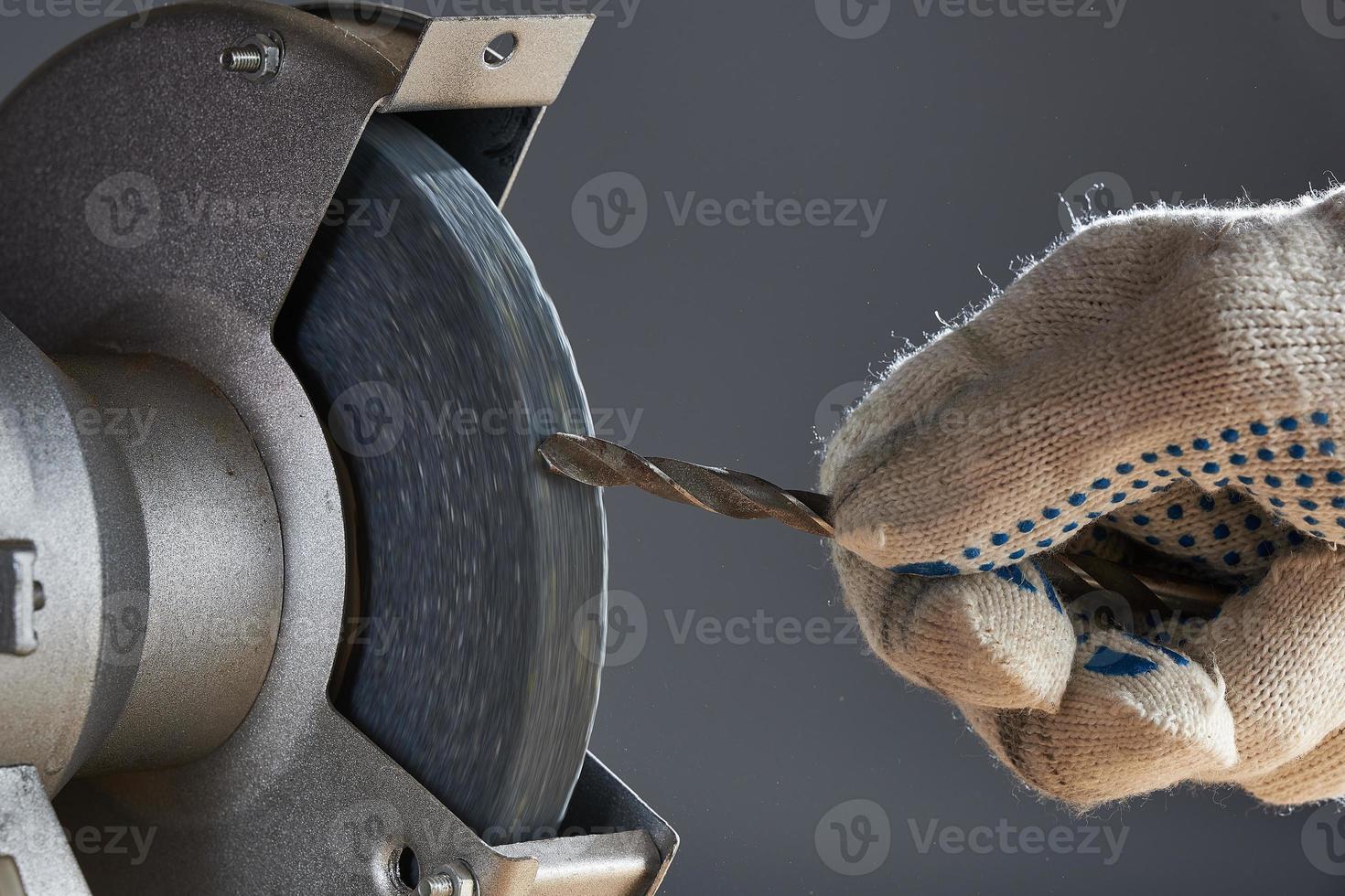 The hand wearing a work glove of man regrinding the drill tool for sharpen the drill tool with grinding wheel. photo