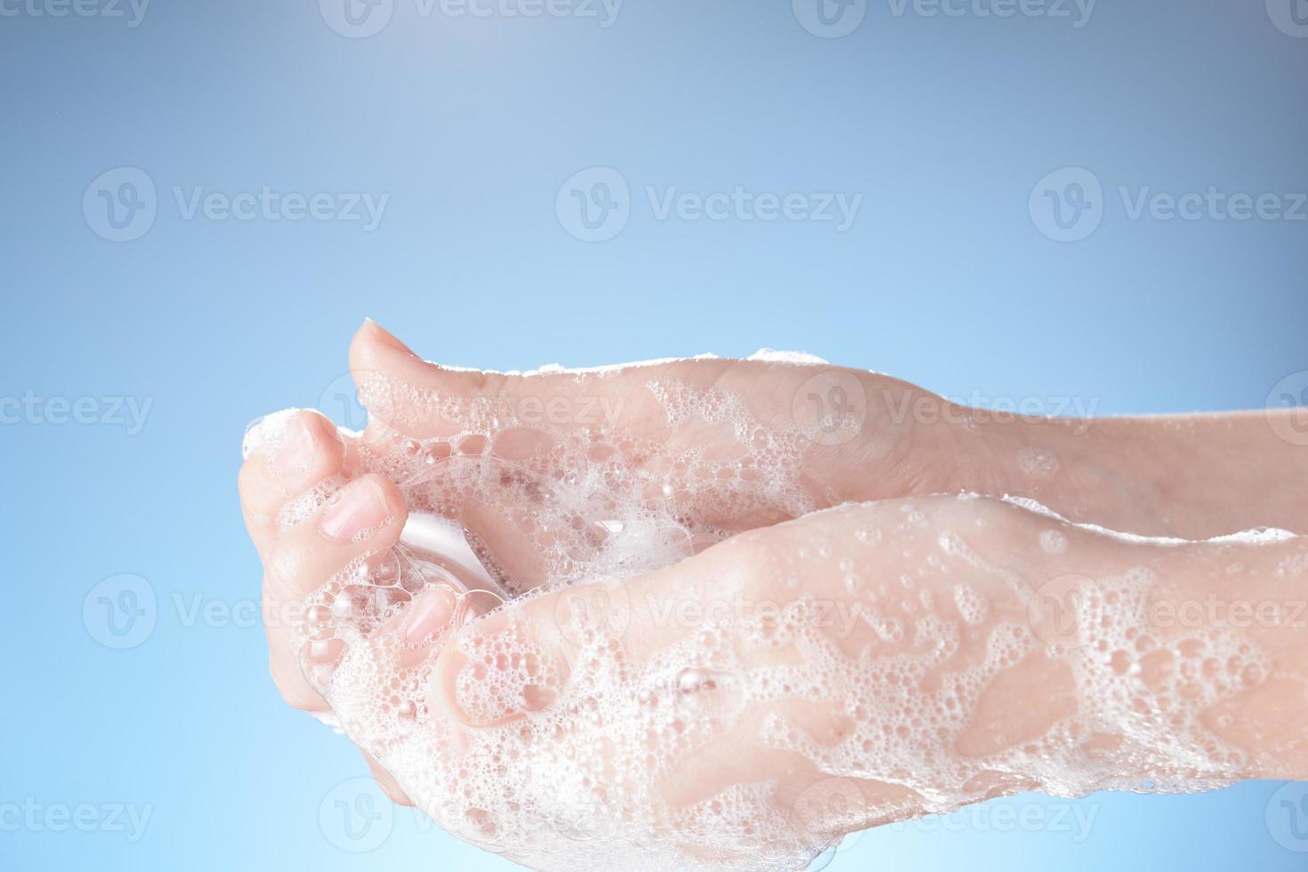 manos de mujer en espuma de jabón, en primer plano de fondo azul. foto