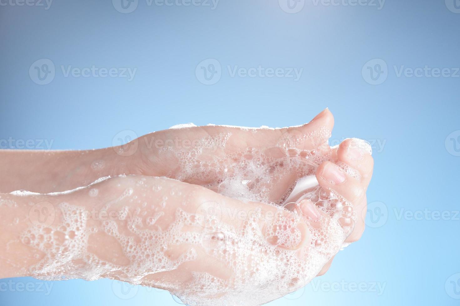 manos de mujer en espuma de jabón, en primer plano de fondo azul. foto