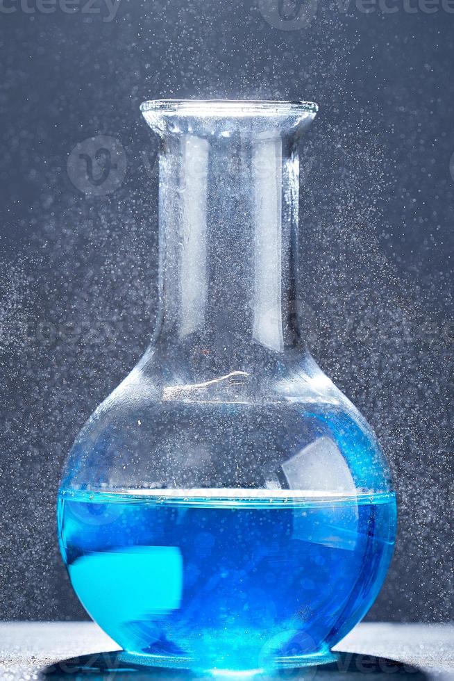 Glass flask with a blue liquid on gray background. photo