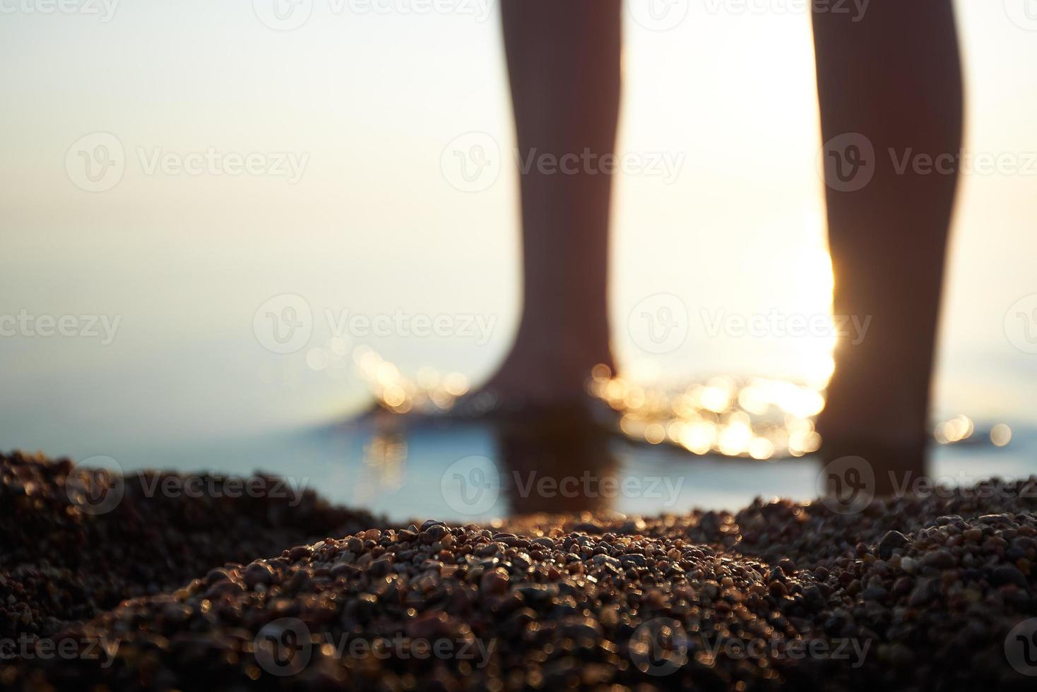 Pebbles on the coast against the background of women's feet in a blur. Girls feet are blurred and out of focus, the sun's rays accentuate the legs. photo