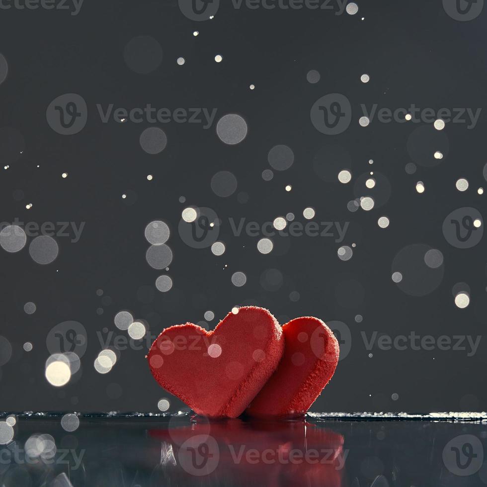 Two red hearts with rain drops reflected in the water on a dark background with a bokeh. Photo with copy space.