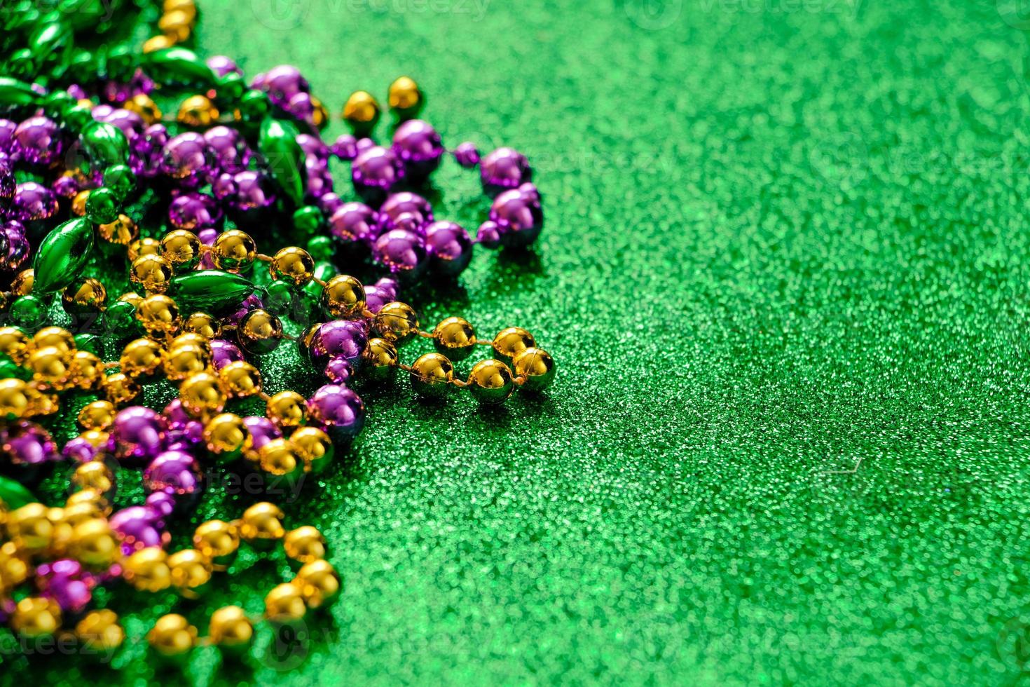 Mardi Gras concept. Multi-colored beads on green shiny background. photo