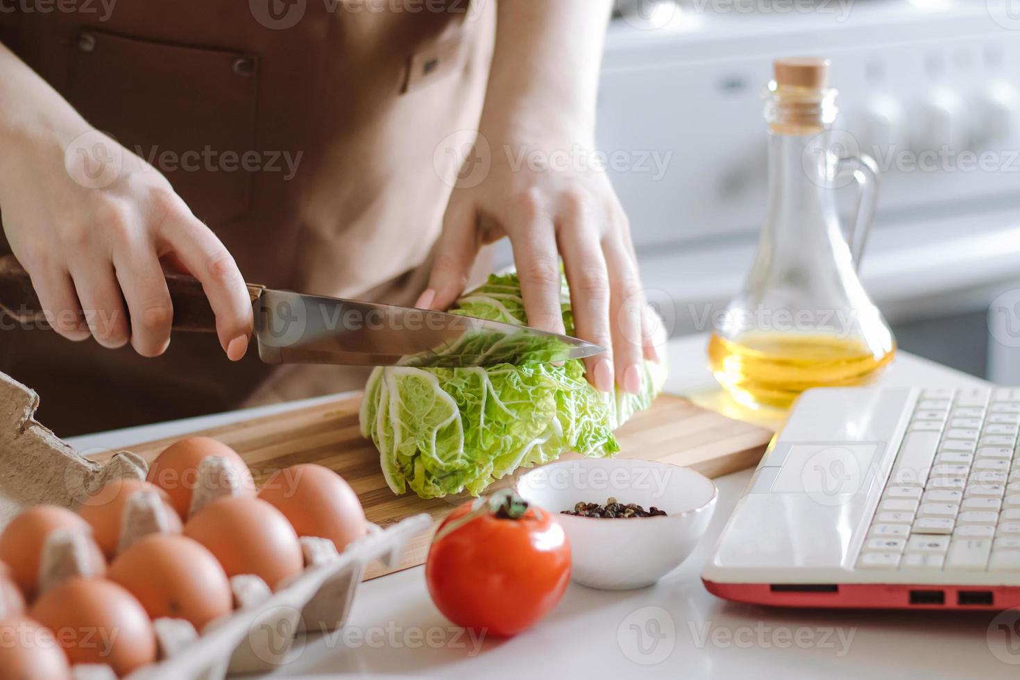 Woman prepares dietary vegetable salad at home using video recipe. photo