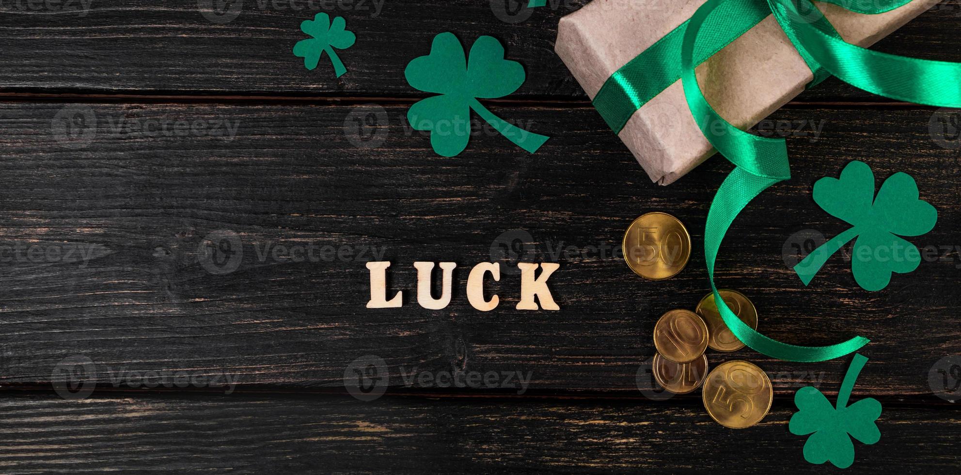 The word luck, clover shamrock and gift with a green ribbon on a dark wooden background. photo