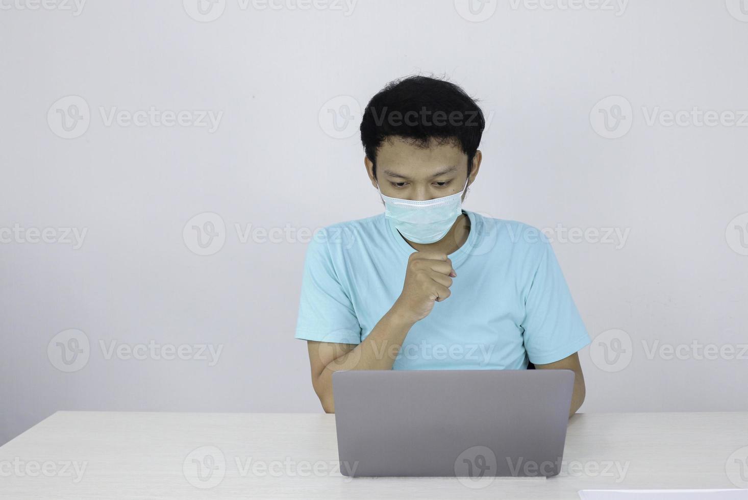 Young Asian man wear medical mask is cough when working with laptop on the table. photo