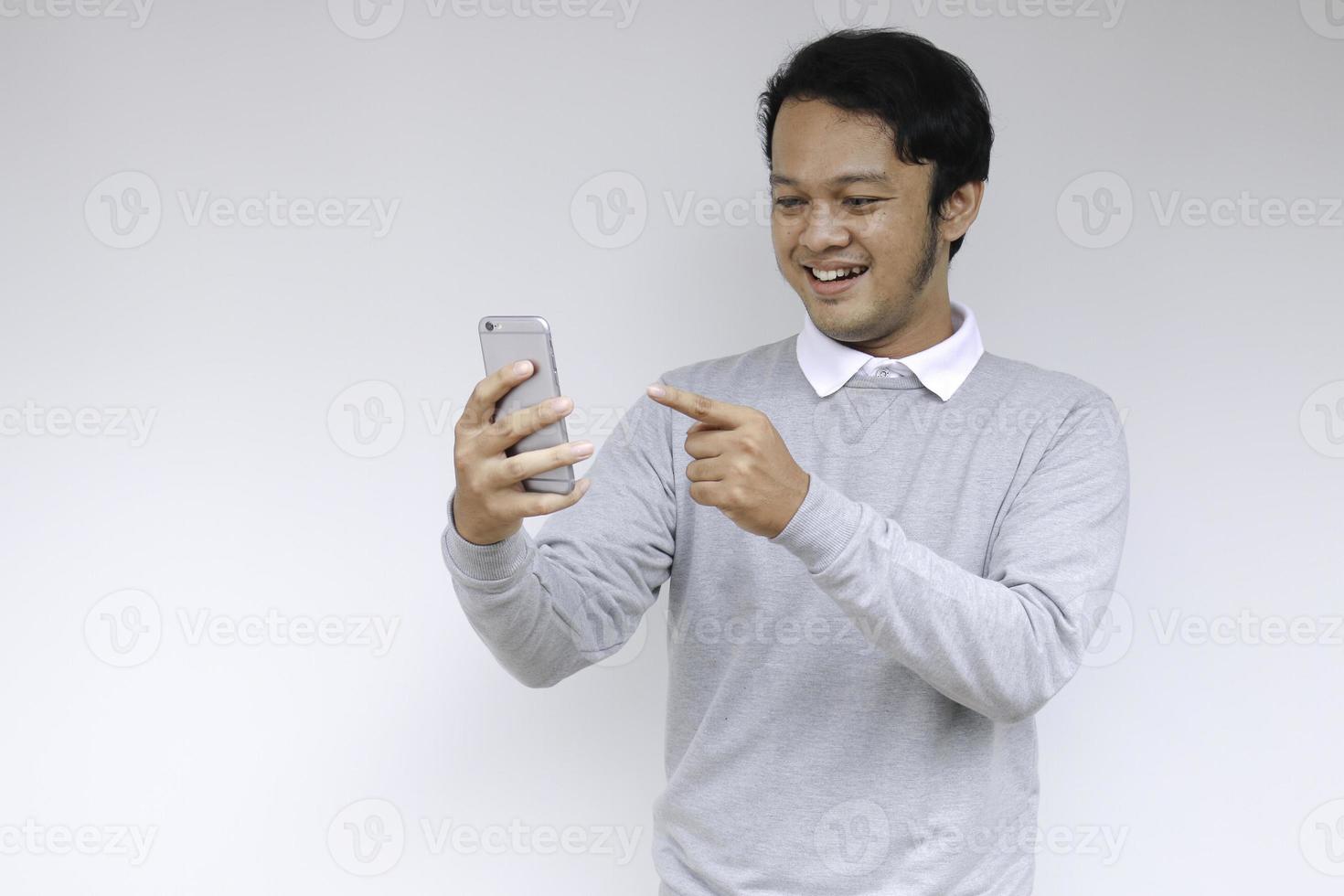 Young Asian man shocked and happy with what he see in the smartphone on isolated grey background. photo